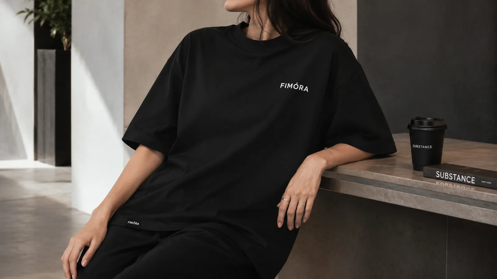 Female model wearing FIMÓRA black T-shirt sitting near coffee table